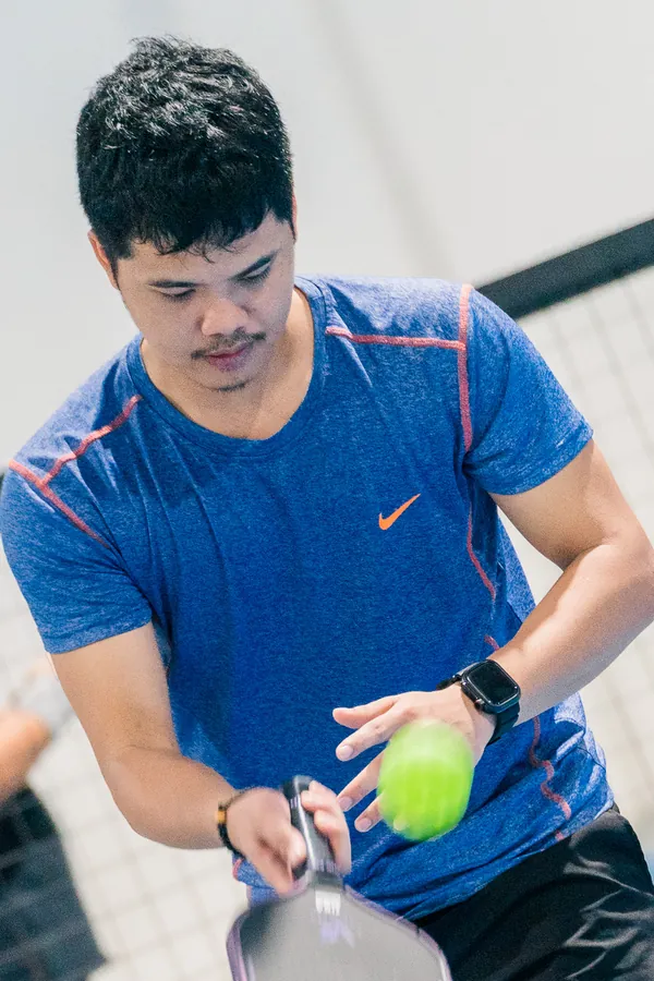 Jayvee Salango getting ready to serve, paddle and ball in hand, on an indoor pickleball court
